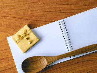 Gold ribbon bow and wooden spoon on blank notepad.