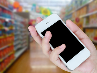 hand holding mobile phone with supermarket shelves aisle blurred