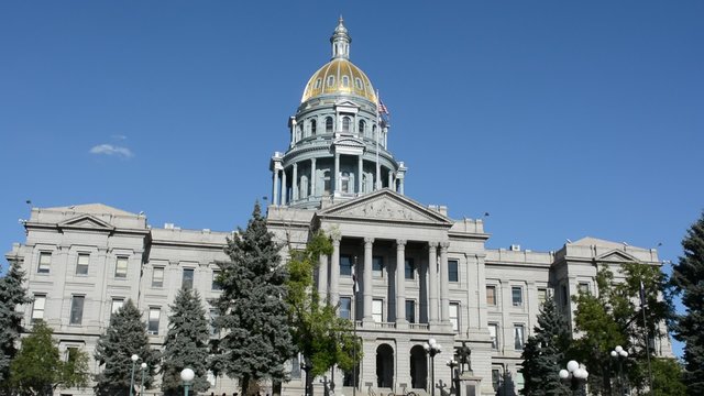 The Colorado Statehouse with an American and Colorado flag on a sunny summer day.