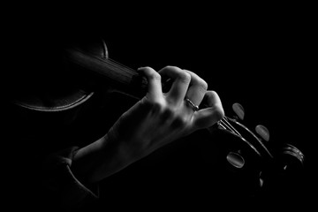 The hand of the musician on the strings of a violin in dark colors on a black background 