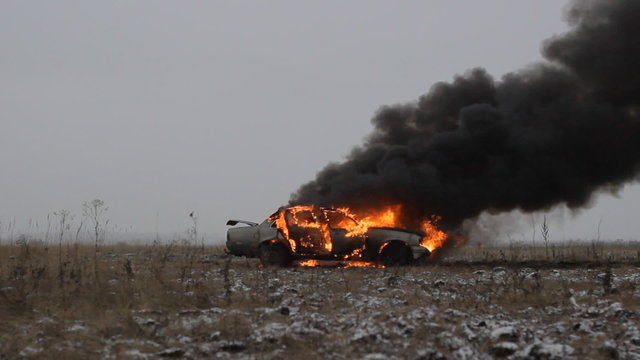 Car on fire on an empty field, side view