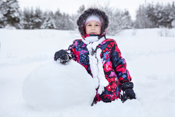 Fototapeta na wymiar Pretty Caucaian girl in winter clothes rolling big snowball for snowman making, winter
