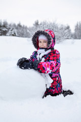 Fototapeta na wymiar Pretty Caucasian girl playing with snowball while making snowman at winter field