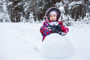 Fototapeta na wymiar Pretty girl in winter clothes rolling snowball for snowman making, winter