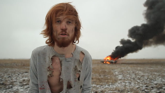 Surviving man on the background of a burning car in the field. Car crash