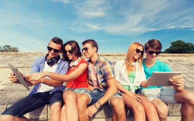 group of smiling friends with tablet pc outdoors