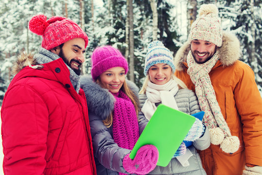 smiling friends with tablet pc in winter forest