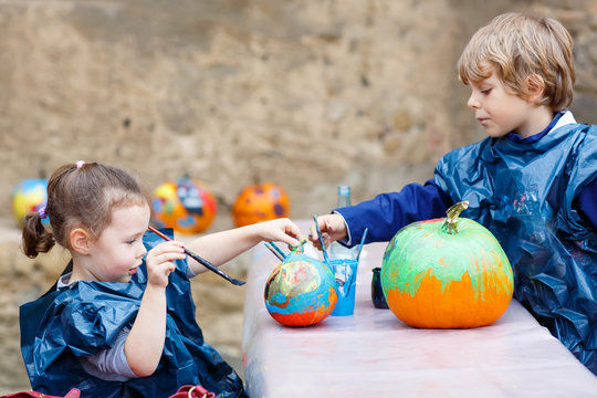 Two little kids painting with colors on pumpkin