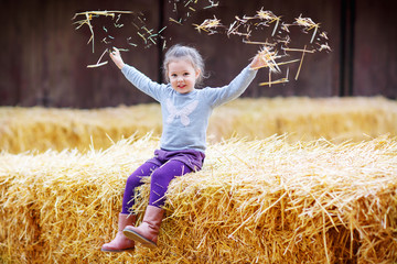 Little cute happy girl having fun with hay on a farm