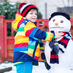 Funny kid boy making a snowman in winter