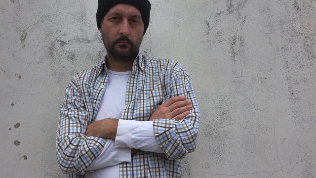 Casual unshaven man looking at camera, thinking, pensive adult man outdoors leaning on the street wall, lifestyle series.
