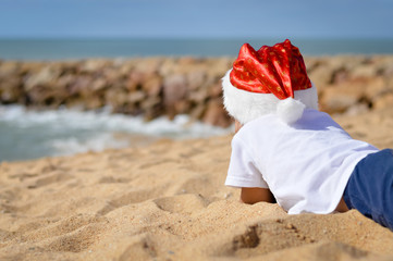 Backview of child in Santa hat lying on sand shore