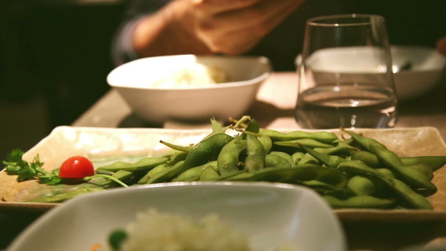 man eating eda mame, a typical japanese food, beans rich in protein and rice at sushi bar