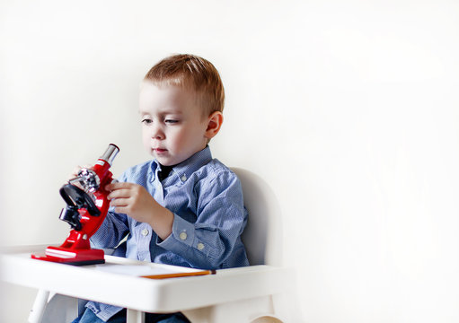 young researcher with a microscope. baby sitting in a high chair and adjusts the microscope