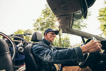 Wide angle shot of senior man driving convertible with bicycle o