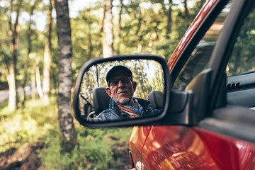 Senior man looking in mirror of car.