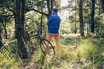 Man standing in forest looking faraway. Bicycle standing against