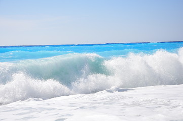 Naklejka na ściany i meble Waves on a sandy beach and a fairytale blue water