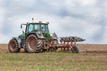Obraz premium Farmer preparing a field for planting - ploughing it with an agricultural plough, close up of the tractor and implement on the skyline