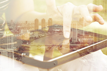 Using digital tablet double exposure and and cityscape background. Business & technology concept.