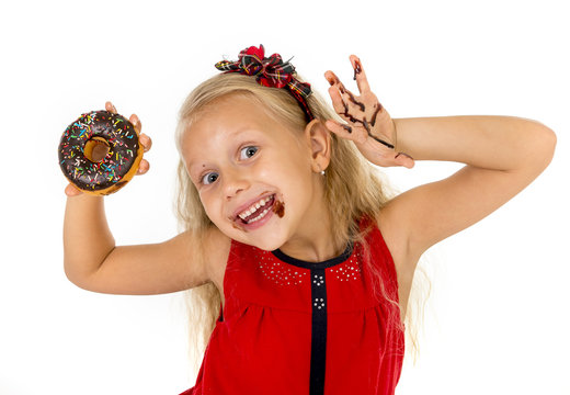 beautiful female child with blue eyes in cute red dress eating chocolate donut with syrup stains