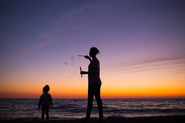 Fototapeta premium Silhouette of Mother and daughter playing with soap bubbles on t