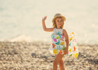 Cute little girl in swimwear waving hand standing on beach, outd