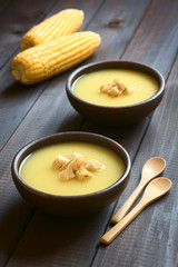 Cream of corn soup with croutons on top, photographed on dark wood with natural light (Selective Focus, Focus on the front of the croutons on the first soup)