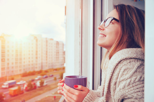cheerful girl drinking coffee in morning sunlight in open window