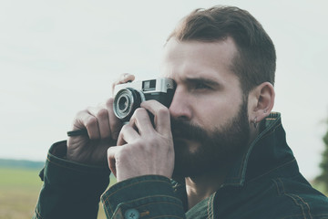 Bearded man holding retro camera and taking photo