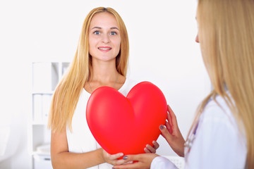 Woman doctor  in  hospital, a large red heart  in patient hand  at the background