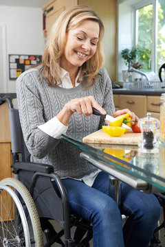 Disabled Woman In Wheelchair Prepapring Meal In Kitchen