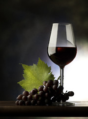 Glass with red wine and grapes on the wooden table