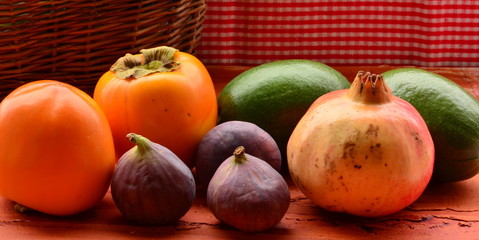 Figs, persimmons, pomegranate and avocados on rough background