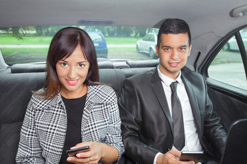 Busy young business people using mobile phones while traveling to work by car