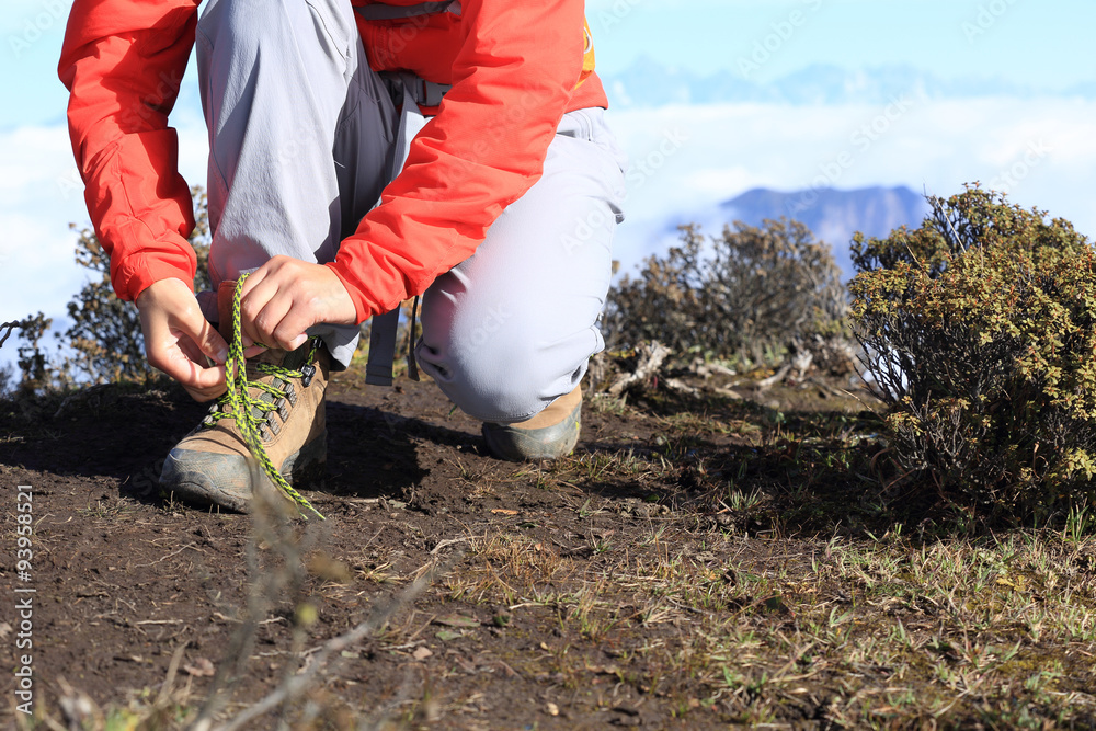 Wall mural hiking woman hiker tying shoelace on beautiful mountain pea