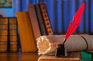 Red quill pen, black inkwell and a rolled papyrus sheet on an old book with a blue background