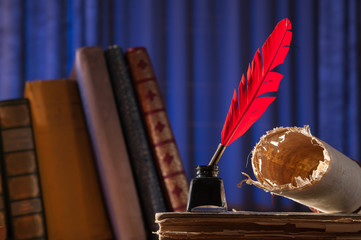 Red quill pen, black inkwell and a rolled papyrus sheet on an old book with a blue background