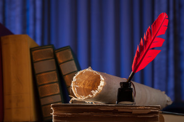 Red quill pen, black inkwell and a rolled papyrus sheet on an old book with a blue background