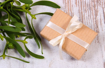 Wrapped gift for Christmas and mistletoe on old wooden background