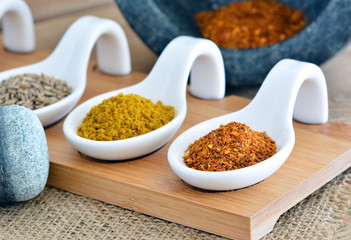 Orientalisches Gewürz - Chili, Curry, Kümmel auf Löffel / Mörser und Stössel auf Jute / Nahaufnahme - Makro