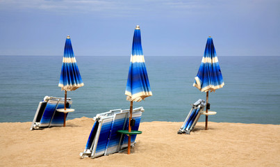 Beach chairs on the sand beach with cloudy blue sky and sun
