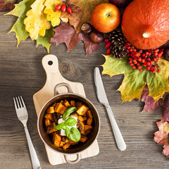 Roasted pumpkin with autumn leaves over wooden background