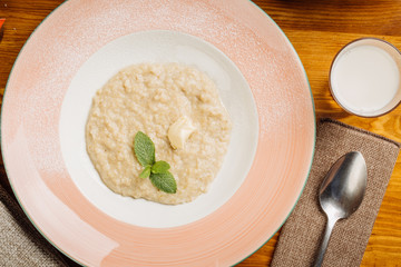 Oatmeal porridge with butter and glass of milk on wooden table