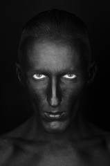 Gothic and Halloween theme: a man with black skin is isolated on a black background in the studio, the Black Death body art