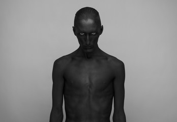 Gothic and Halloween theme: a man with black skin is isolated on a gray background in the studio,...