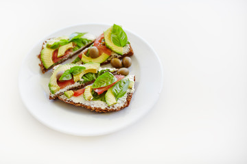 Sliced avocado on toast bread. Sandwich with cheese, tomatoes, olives and basil