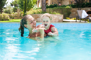 Happy young active mother and  curly little baby having fun in a swimming pool