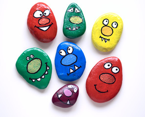 Seven smiling faces of monsters. Painted acrylic pebbles.