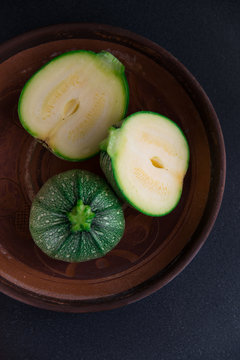 Round courgette zucchini on dark background in a terracotta dish (top view, natural light)